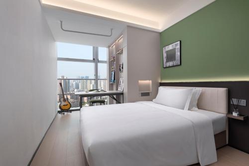 a bedroom with a white bed and a desk with a guitar at Modena By Fraser Shenzhen in Shenzhen