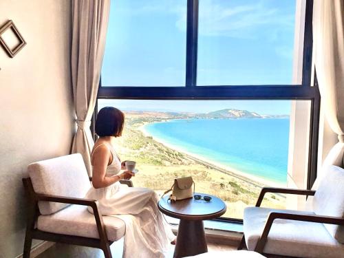 a woman sitting in a chair looking out a window at the beach at Mũi Né Luxury- View sea Apec in Ấp Thiẹn Ái