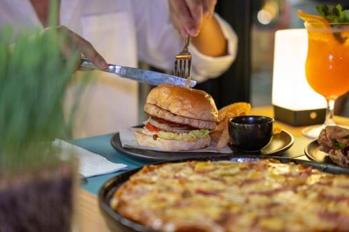 a person cutting a sandwich on a table with a pizza at Wyndham Garden Naithon Phuket in Nai Thon Beach
