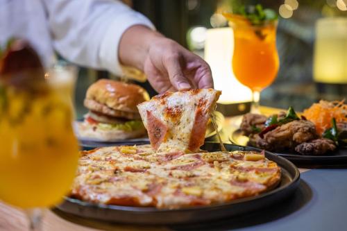 a person eating a slice of pizza on a table with food at Wyndham Garden Naithon Phuket in Nai Thon Beach