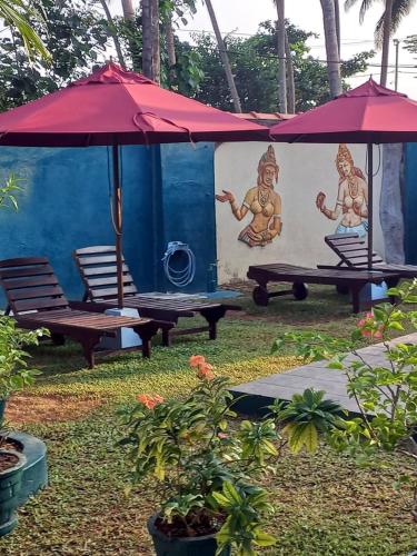 two benches with umbrellas in front of a house at Sankarest Villa in Kosgoda