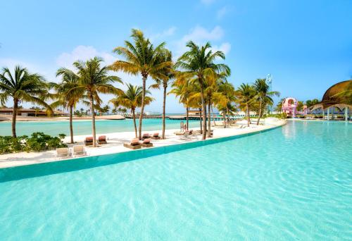 a pool at a resort with palm trees and chairs at Centara Mirage Lagoon Maldives in Nakachchafushi
