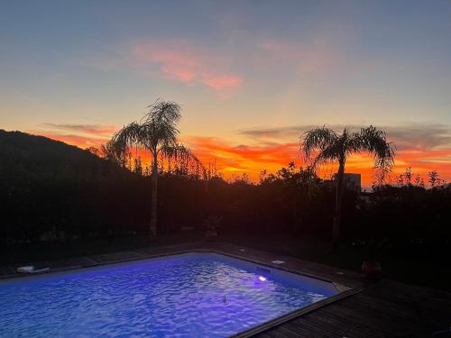 a large swimming pool with a sunset in the background at Magnifique villa récente entre mer et montagne située entre Ajaccio et Porticcio in Cauro