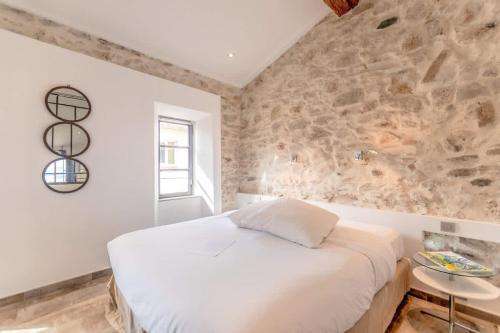 une chambre avec un lit blanc et un mur en pierre dans l'établissement Loft Allard l Harbour Views l Shellter Rentals, à Saint-Tropez