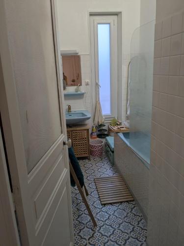 d'une salle de bains avec une porte s'ouvrant sur une salle de bains pourvue d'un lavabo. dans l'établissement Grand F3 Clermont Ferrand Centre et Garage salins, à Clermont-Ferrand