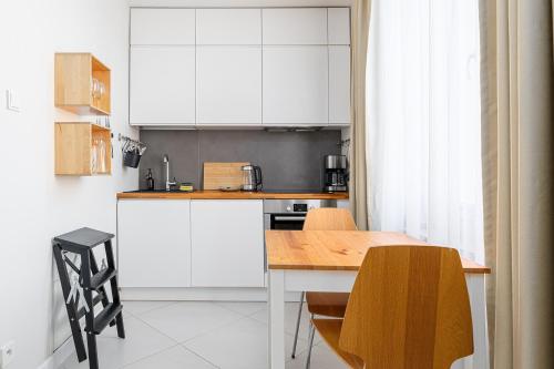 a kitchen with white cabinets and a wooden table at RentPlanet - Studio Białobrzeska in Warsaw