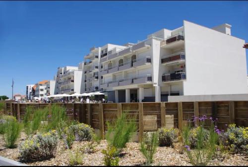 Un edificio con una valla y flores delante. en Studio cosy au porte de l ocean, en Biscarrosse