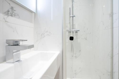 La salle de bains est pourvue d'une douche et de murs en marbre blanc. dans l'établissement Charmant appartement centre Paris 2 - 2P, à Paris