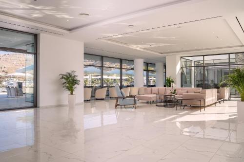 a lobby with couches and tables and windows at Lindos Grand Resort & Spa - Adults Only in Líndos