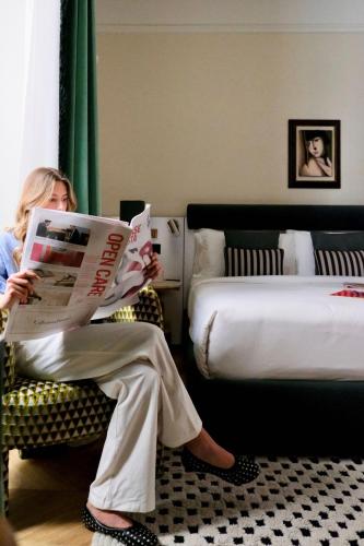 a woman sitting in a chair reading a newspaper in a hotel room at The Couper Umiltà in Rome