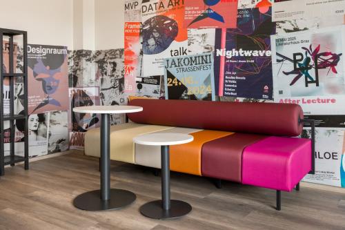a colorful bench in a room with two tables and posters at a&o Graz Hauptbahnhof in Graz