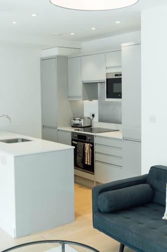 a kitchen with white cabinets and a blue couch at Access Brick Lane in London