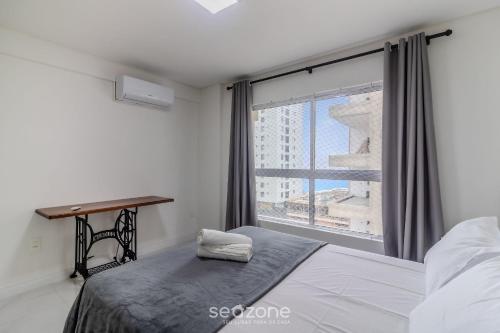 a bedroom with a bed and a window with a desk at Apto com vista incrível a 230m do Mar - MRE1101 in Perequê
