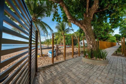 a fence with a tree next to a sidewalk at Luxo e Tranquilidade na Ponta do Mutá - 2 Suítes em Cond Pé na Areia! in Barra Grande