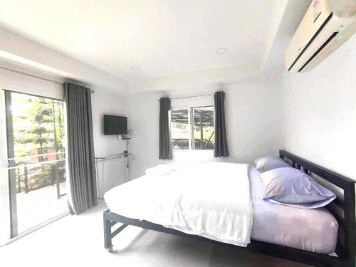 a white bedroom with a bed and a large window at น้ำหนาวโฮมสเตย์เขาค้อ2 in Campson