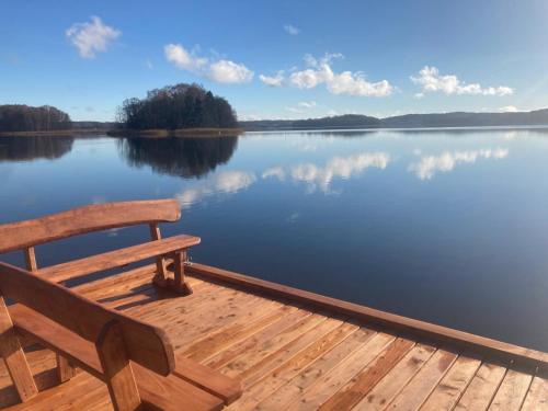 a wooden bench sitting on a dock next to a lake at Ceglany Domek z jacuzzi, nad jeziorem, przy lesie in Tomaszkowo