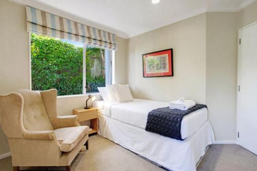 a bedroom with a bed and a chair and a window at Wonderful Guest Suite Steps to St Heliers Beach in Auckland