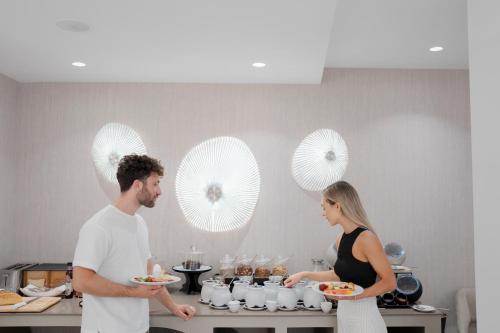 a man and a woman holding plates of food in a kitchen at Ethereal White Resort Hotel & Spa - Adults Only in Heraklio Town