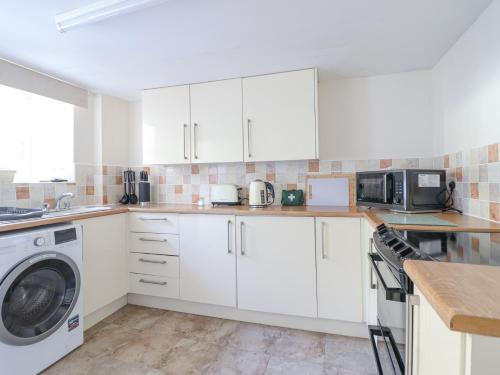 a kitchen with white cabinets and a washer and dryer at Minffordd in Abergele