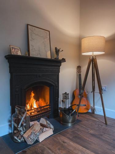 a living room with a fireplace and a lamp and a guitar at Chapel Cottage- Coastal Somerset Retreat in Williton