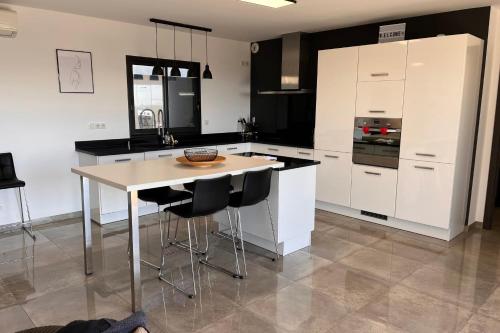 une cuisine avec des placards blancs et un îlot avec des tabourets de bar dans l'établissement Romane - Terrace Garden Great View - by TGB, à Alata