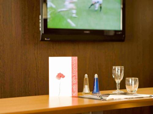 a table with a television and two glasses and a menu at Hotel Mermoz Paris Le Bourget in La Courneuve