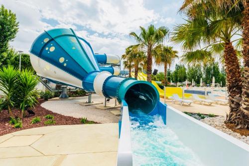 un toboggan bleu dans un complexe avec des palmiers dans l'établissement Mobilhome la Carabasse 40m2 6-8 personnes, à Vias