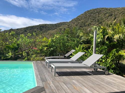 a group of lounge chairs next to a swimming pool at Villa Bambou, vue mer, panorama sur la baie des Saintes in Terre-de-Bas