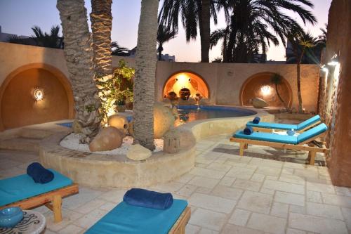 una piscina con palmeras y bancos con cojines azules en Rêve à Djerba - Dar El Mina, en Houmt El Souk