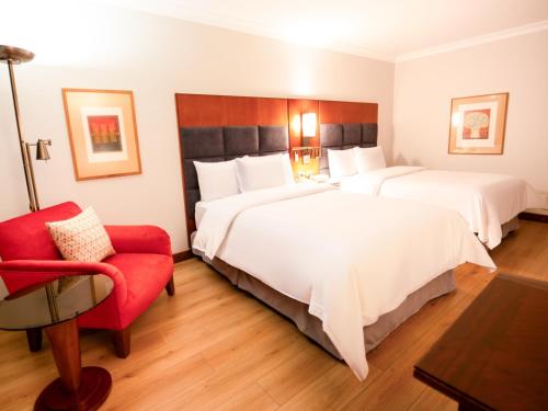 a hotel room with two beds and a red chair at Swissotel Quito in Quito