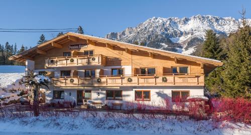 a large wooden house in the snow with a mountain at Pension Aloisia in Scheffau am Wilden Kaiser