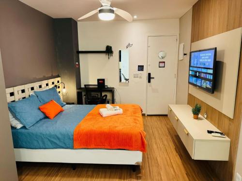 a bedroom with a bed with an orange blanket and a tv at Modern Studio in Catete – Close to the Metro in Rio de Janeiro
