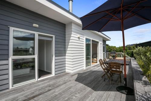 a wooden deck with a table and an umbrella at Sandy Serenity in Waihi Beach