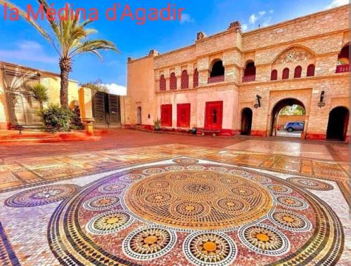 a mosaic floor in front of a building with a palm tree at Maison pres plus Grand Bazar d'Afrique Souk El Had in Agadir