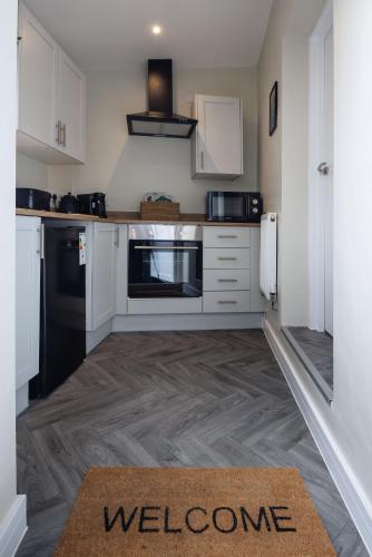 a kitchen with white cabinets and a welcome sign on the floor at 4 Bedroom, Sleeps 8, 3 Bathroom, Hot Tub, WiFi, Smart TVs in Each Room 3 min walk to KINGSHOLM Stadium in Gloucester