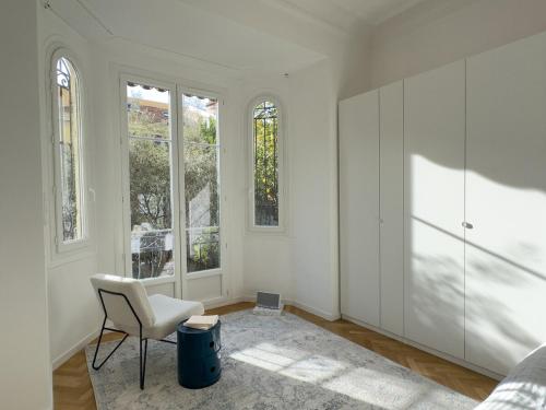 Cette chambre blanche dispose d'une chaise et de quelques fenêtres. dans l'établissement Nice Cote d'Azur jardin parking 6 pers luxe, à Nice