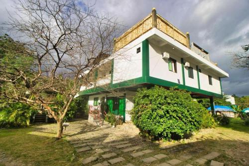 a green and white house with a tree in front of it at Casa Luntian Lodge and Cafe in Puerto Galera