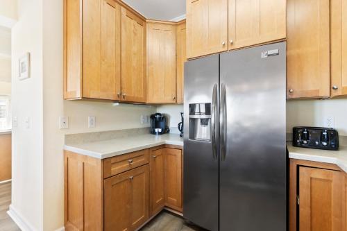 a kitchen with wooden cabinets and a stainless steel refrigerator at Oceanview 4BR/4BA Condo, Steps to Beach/Pool in Ocean Isle Beach