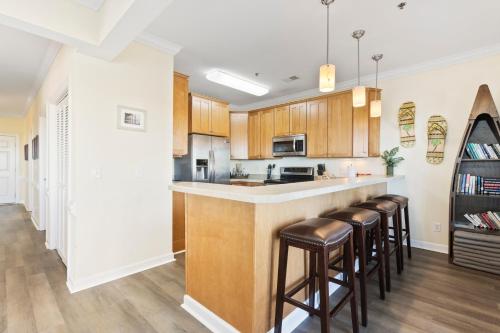 a kitchen with wooden cabinets and a bar with stools at Oceanview 4BR/4BA Condo, Steps to Beach/Pool in Ocean Isle Beach