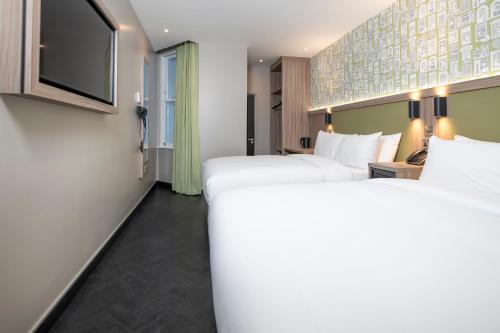 a hotel room with two beds and a flat screen tv at Brit Hotels Earls Court in London