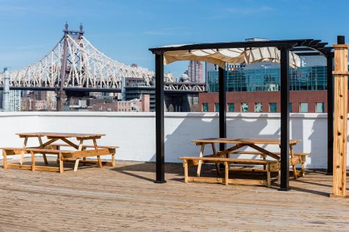 a group of picnic tables on a boardwalk with a bridge at LIC Hotel in Queens