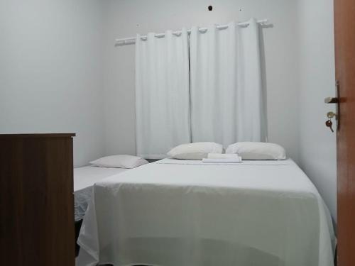 a white bedroom with two beds with white sheets at Casadapraça in Goianésia