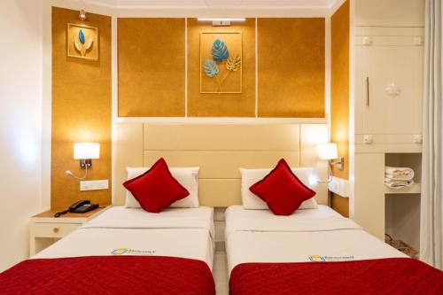 two beds in a hotel room with red pillows at Excellency Airport Hotel in Angamali