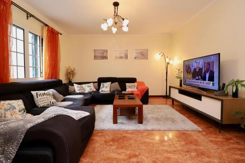 a living room with a black couch and a tv at Villa Rose by AnaLodges in São Vicente