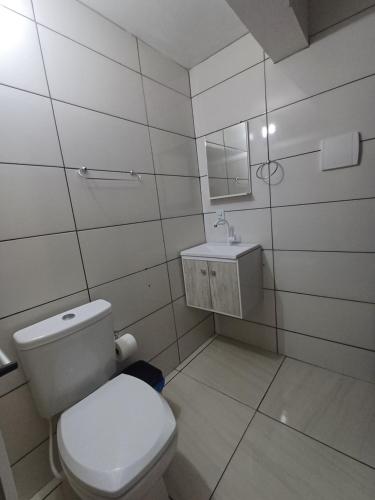 a white bathroom with a toilet and a sink at Suite Térrea in Bombinhas