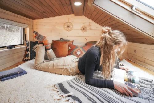 a woman laying on the floor in a tiny house at Thistle House at Camp Greenwood Vermont with Sauna in Chester
