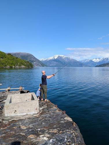 a man standing on the edge of a lake holding a fishing rod at Charming guest house with amazing view in Kvam