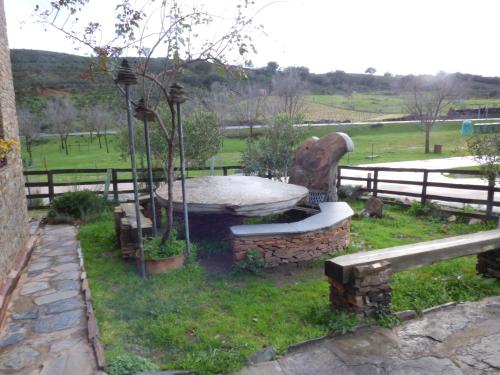 a stone fountain in the grass next to a fence at Casa Rural Al-Mofrag y Apartamentos El Mirador de Monfragüe in Villarreal de San Carlos