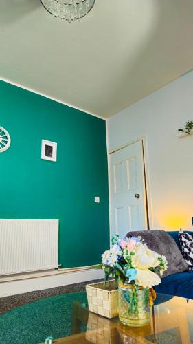 a living room with a green wall and a table with flowers at IVY GREEN HOUSE - STYLISH VALUE STAY, SLEEPS upto 7, LUXURY BEDS, CENTRAL, WIFI, NETFLIX, FREE PARKING in Derby