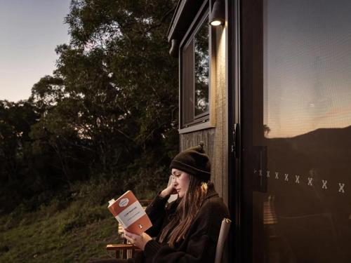 a woman sitting in a chair reading a book at Off-Grid Cabin Surrounded by Nature - Hot Tub - Banjo in Jamberoo
